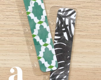 Może przedstawiać: Dwa przezroczyste plastikowe separatory do planera z dekoracyjnymi wkładkami. Jedna wkładka ma zielono-biały geometryczny wzór, druga czarno-biały abstrakcyjny wzór. Litera "a" znajduje się w lewym dolnym rogu.