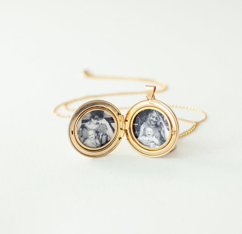 Peut inclure: Un pendentif m&eacute;daillon circulaire dor&eacute; sur une fine cha&icirc;ne assortie. Le m&eacute;daillon est ouvert, r&eacute;v&eacute;lant deux photographies circulaires en noir et blanc &agrave; l'int&eacute;rieur. Une photo montre un adulte tenant un b&eacute;b&eacute;, l'autre un adulte souriant avec un b&eacute;b&eacute;.