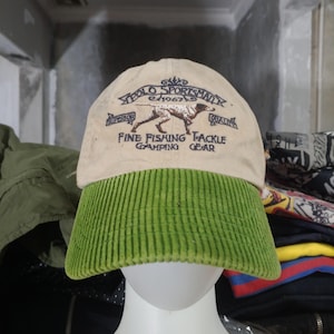 Puede incluir: Gorra beige Polo Sportsman con visera de pana verde. La gorra presenta texto bordado y un gráfico de perro. El texto dice "POLO SPORTSMAN" y "FINE FISHING TACKLE CAMPING GEAR".