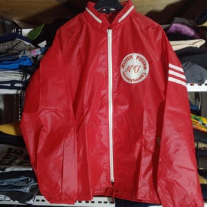 May include: Red nylon jacket with a white zip, collar trim, and sleeve stripes. The jacket features a circular logo with the text "Auster Pulsar N.T. Cherry Vanette". The jacket is hanging on a black hanger.
