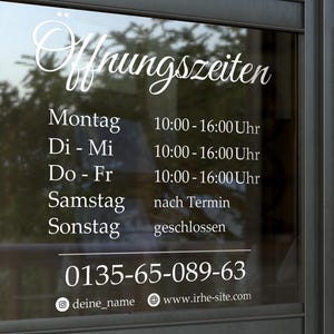 Op de afbeelding: Een glazen deur met witte tekst die openingstijden aangeeft. De tekst bevat het woord "Offnungszeiten", dagen van de week en tijden. Een telefoonnummer en websiteadres zijn ook zichtbaar.