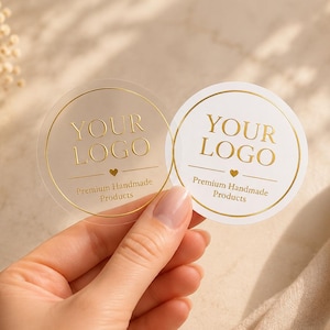 May include: Two circular stickers featuring gold foil text that reads YOUR LOGO and Premium Handmade Products with a small heart icon. One sticker is transparent and the other is opaque white, both framed by a thin gold circular border.