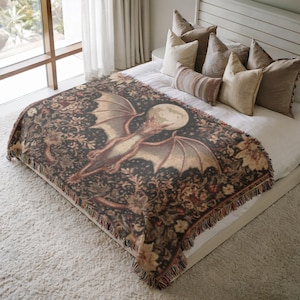May include: A woven throw blanket featuring a dragon with outstretched wings, a full moon, and floral patterns in shades of brown, beige, and black. The blanket has a fringed edge and is displayed on a bed with pillows.