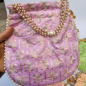 Könnte beinhalten: Ein lavendelfarbener Kordelzugbeutel mit aufwendigen Stickereien und Paillettendetails. Die Tasche hat ein Blumenmuster und ist mit einem perlenbesetzten Riemen und Besatz verziert. Die Tasche ist ca. 15 cm breit und 18 cm hoch.