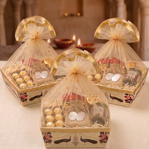 May include: Three square gift baskets wrapped in sheer gold-trimmed tulle, each containing gold-wrapped chocolates, a small beige drawstring pouch with silver coins, and a glass jar. The baskets feature a decorative peacock and floral print.