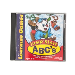 May include: A JumpStart ABC's CD-ROM game case for ages 3-5. The cover features a cartoon polar bear sledding in the snow with a rabbit. Text includes "Learning Games," "JumpStart ABC's," "Learn ABC's and Pre-Reading Skills," and system requirements.
