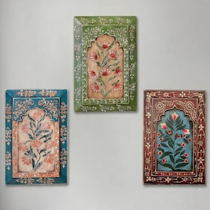 May include: Three rectangular wall art pieces with floral designs. The frames are painted in teal, green, and maroon, with intricate patterns. The central panels feature stylized flowers in red and white against a beige and blue background.