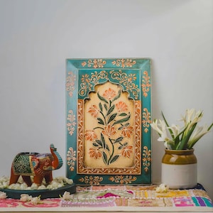 May include: A teal and orange floral wall art piece with a cream-colored center. The art is framed and features a floral design. An elephant candle holder and a vase of white flowers are also present.