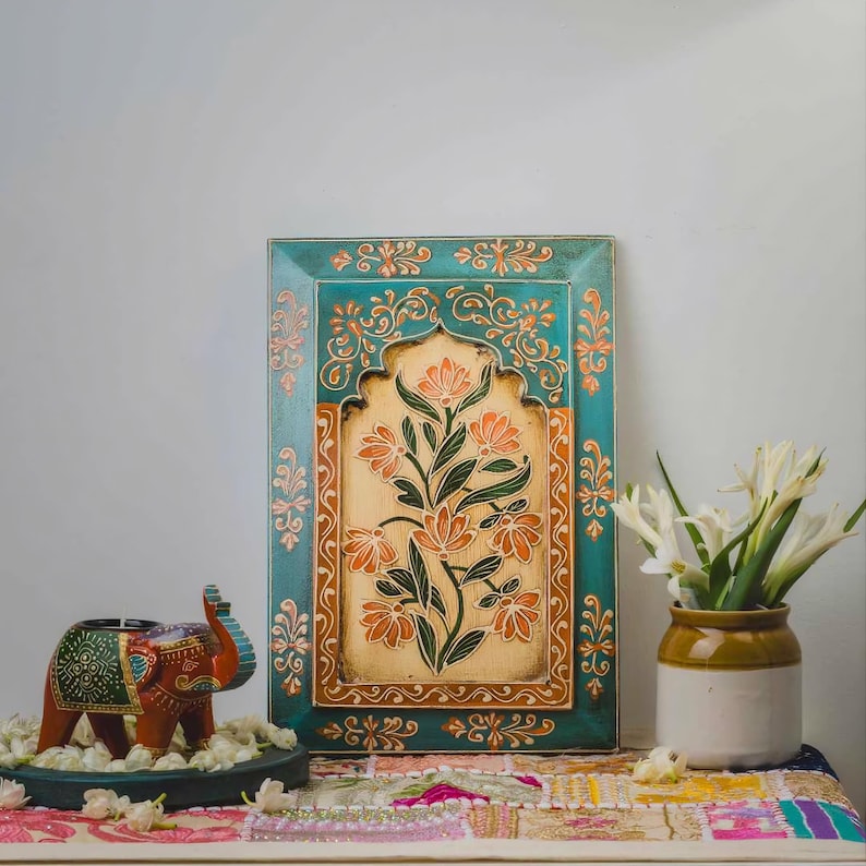 May include: A teal and orange floral wall art piece with a cream-colored center. The art is framed and features a floral design. An elephant candle holder and a vase of white flowers are also present.