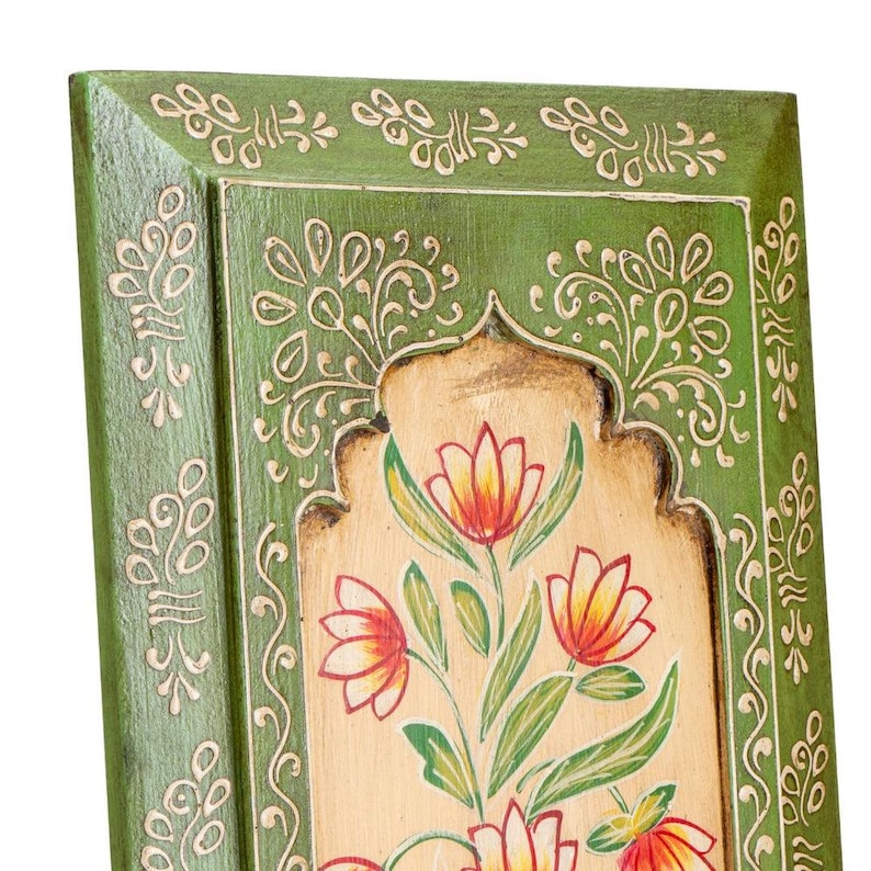 May include: A hand-painted wooden panel with a green frame and floral design. The panel features a beige background with red, yellow, and green flowers. Intricate white scrollwork decorates the frame and the central design, creating a decorative piece.