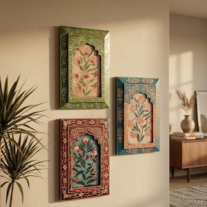 May include: Three framed floral art pieces in shades of green, teal, and burgundy hang on a beige wall. Each frame has an arched top and intricate floral designs. The artwork features stylized flowers.