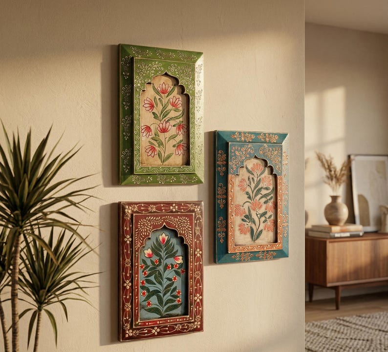 May include: Three framed floral art pieces in shades of green, teal, and burgundy hang on a beige wall. Each frame has an arched top and intricate floral designs. The artwork features stylized flowers.