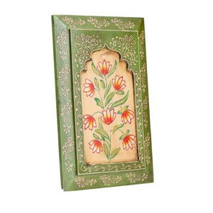May include: A rectangular, wooden wall art piece with a green frame and floral design. The central panel features a beige background with a painted floral arrangement in red, orange, and green. The frame has a decorative, carved pattern.