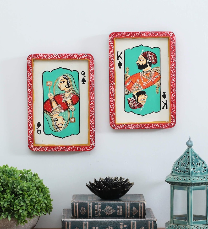 K&ouml;nnte beinhalten: Zwei gerahmte Spielkarten-Kunstwerke. Eines zeigt eine K&ouml;nigin in Rot und Gold, das andere einen K&ouml;nig in Orange und Gold. Beide Karten haben einen t&uuml;rkisfarbenen Hintergrund und rote Rahmen mit wei&szlig;en floralen Details. Das Kunstwerk wird an einer wei&szlig;en Wand ausgestellt.