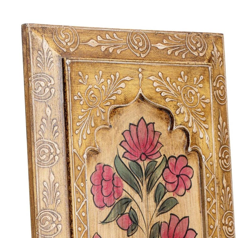 May include: Close-up of a decorative wooden panel with a gold-coloured frame and floral design. The panel features a central floral motif with pink flowers and green leaves, set against a light-coloured background. Intricate white carvings adorn the frame.