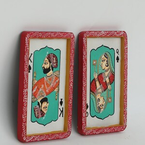 K&ouml;nnte beinhalten: Zwei gerahmte Spielkarten-Kunstwerke. Eines zeigt einen K&ouml;nig in Orange und Gold, das andere eine K&ouml;nigin in Rot und Gold. Beide haben einen t&uuml;rkisfarbenen Hintergrund und sind rot mit wei&szlig;en floralen Akzenten gerahmt.