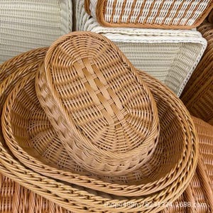May include: A collection of oval-shaped woven baskets featuring a light brown, natural-toned finish. The baskets are constructed with a tight, uniform weave pattern and a reinforced braided rim, stacked together to display their structural design.