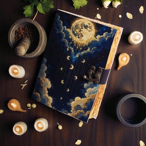 May include: A journal with a celestial design featuring a full moon, crescent moons, and clouds. The cover is dark blue with gold and white accents. The journal is open, revealing aged paper. Small candles and a mortar and pestle surround the journal.