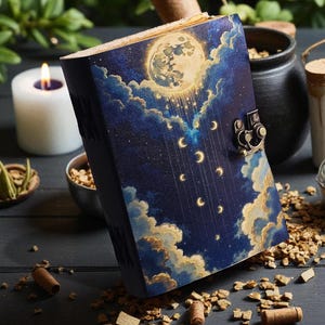 May include: A hardcover journal with a celestial design featuring a full moon, clouds, and crescent moons against a dark blue background. The journal has a metal clasp and is surrounded by candles and herbs.