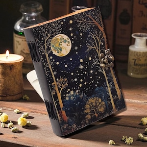 Puede incluir: Un diario decorativo con un diseño de bosque celestial. La portada presenta una luna llena, estrellas y árboles en tonos dorados y azules sobre un fondo azul oscuro. Tiene un cierre de metal y una encuadernación cosida.