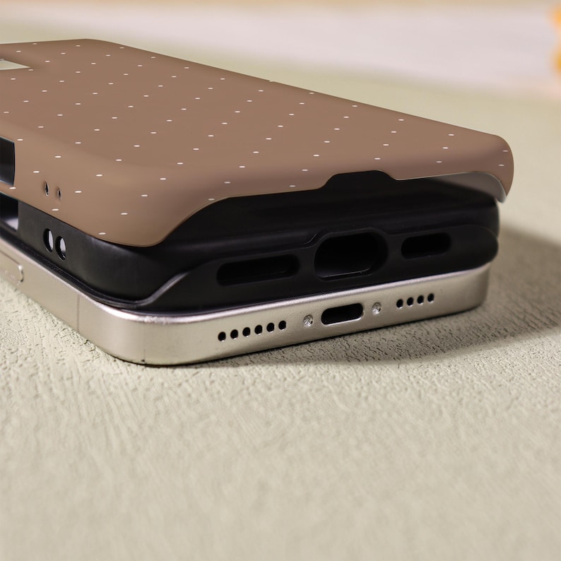 May include: A stack of three phone cases. The top case is brown with a pattern of small white dots. The middle case is black, and the bottom case is silver. The cases are stacked on top of each other.