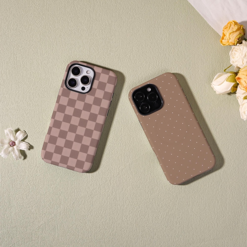 May include: Two phone cases with different designs. One case has a brown and tan checkerboard pattern. The other case is a solid brown color with small white polka dots. Both cases have a black camera lens cutout.