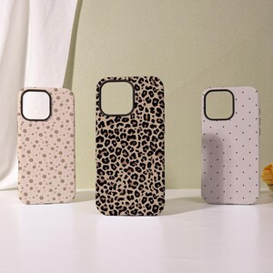 May include: Three phone cases with different patterns. The first case is light pink with small, brown floral designs. The second case has a leopard print pattern in brown and black. The third case is light pink with small, black polka dots.