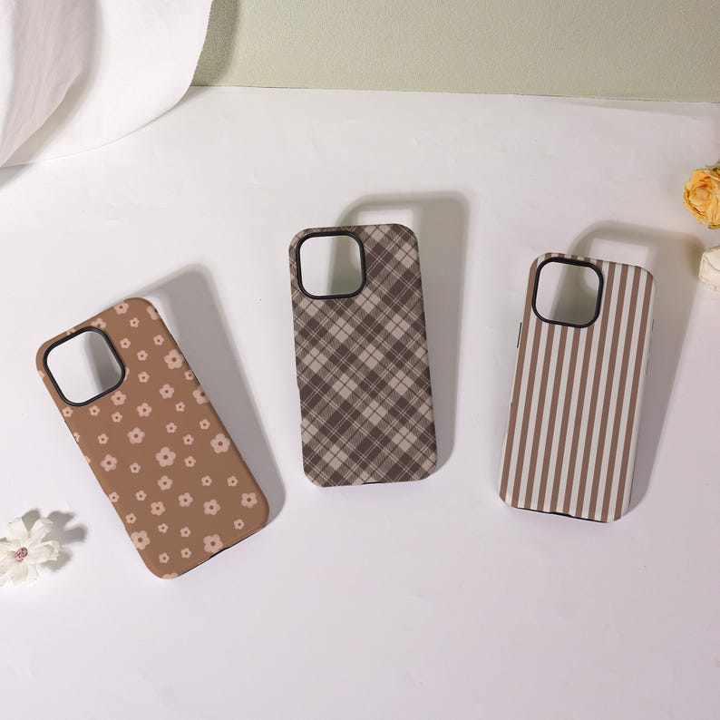 May include: Three phone cases with different designs. One case is brown with small white flowers, another is brown plaid, and the third is brown and white vertical stripes. All cases have black borders.