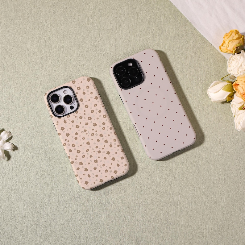 May include: Two phone cases with floral and polka dot patterns. One case has a beige background with small brown flowers. The other case has a light gray background with small black dots. Both cases have black camera cutouts.
