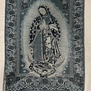May include: A teal and grey tapestry depicting the Virgin Mary with a halo and clasped hands. The tapestry has a floral border and fringe at the bottom. The image is centered on a white background.