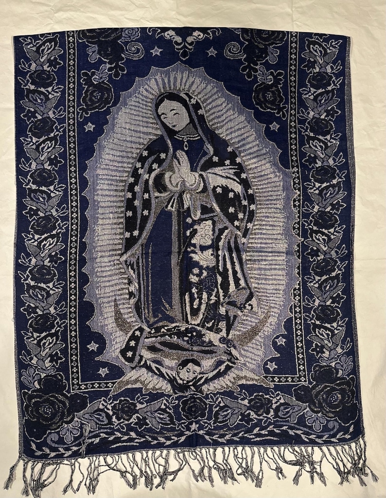 May include: A navy blue tapestry depicting the Virgin Mary in prayer. The tapestry has a floral border and fringe along the bottom. The image is in shades of blue, grey, and black. The tapestry is suitable for wall decor.