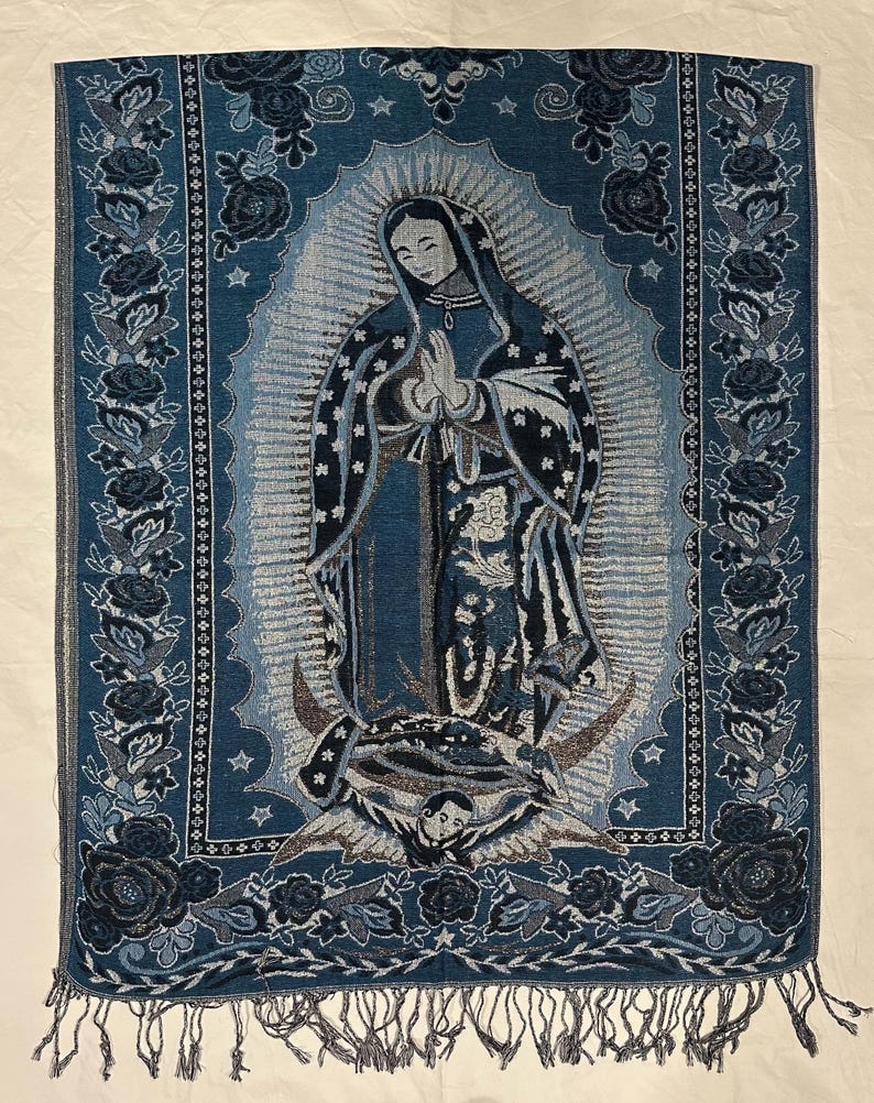 May include: Blue tapestry depicting the Virgin Mary with a halo, framed by floral and star motifs. The tapestry, with a fringed border, is mainly blue with white and grey highlights. The measurements are in centimeters.