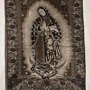 May include: A brown and grey tapestry depicting the Virgin Mary with a halo, stars, and a crescent moon. The tapestry has a floral border and fringe at the bottom. The image is a religious depiction.