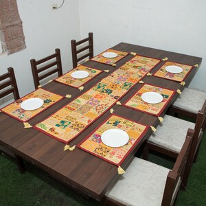 Puede incluir: Una mesa de comedor rectangular de madera marr&oacute;n oscuro con seis sillas con cojines claros. La mesa est&aacute; decorada con un camino de mesa de patchwork largo y seis manteles individuales rectangulares a juego, cada uno con un plato blanco.
