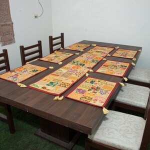Puede incluir: Un juego de mesa de comedor rectangular que incluye un camino de mesa central largo y seis manteles individuales rectangulares a juego. Cada pieza est&aacute; hecha de un mosaico de cuadrados de tela multicolor con bordados y borlas amarillas.