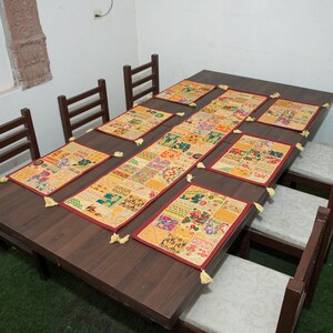Puede incluir: Un camino de mesa rectangular y seis manteles individuales rectangulares a juego con un dise&ntilde;o de patchwork de varios patrones florales y geom&eacute;tricos en tonos amarillo, naranja, rojo y verde, terminados con peque&ntilde;as borlas amarillas.