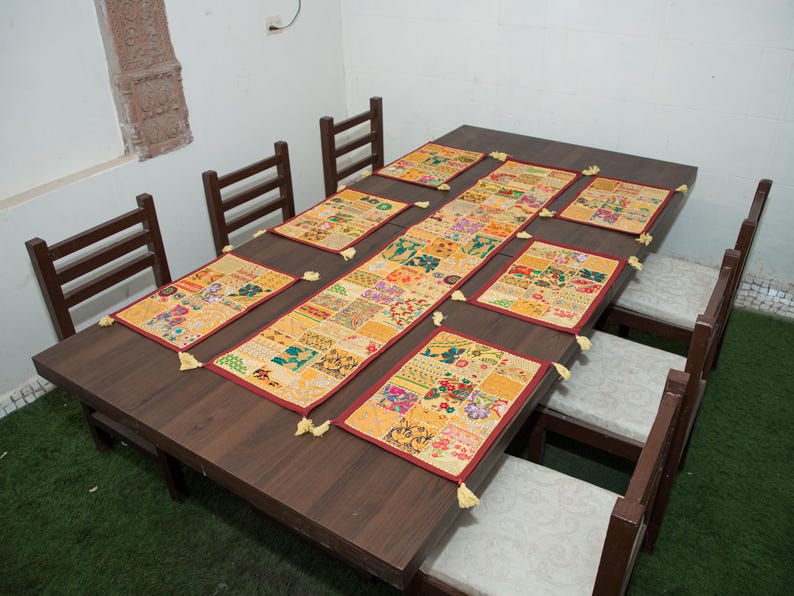 Puede incluir: Un camino de mesa rectangular y seis manteles individuales rectangulares a juego con un dise&ntilde;o de patchwork de varios patrones florales y geom&eacute;tricos en tonos amarillo, naranja, rojo y verde, terminados con peque&ntilde;as borlas amarillas.
