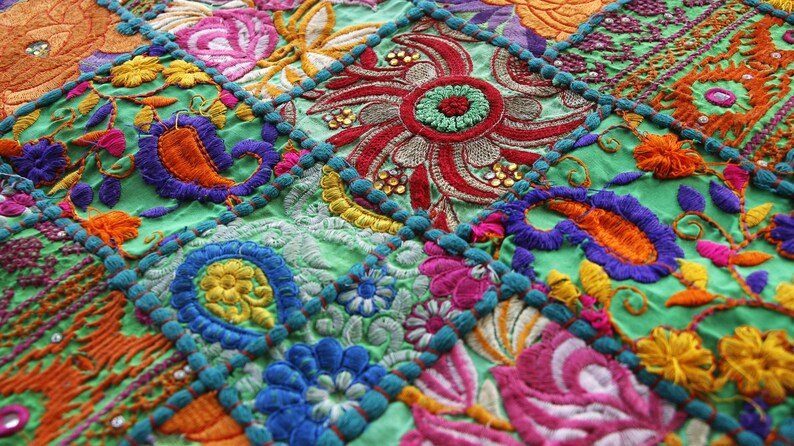 May include: A patchwork textile featuring a vibrant green base fabric with intricate multi-coloured embroidery. The design includes floral motifs, paisley patterns, and circular shapes accented with small reflective sequins and raised stitching.