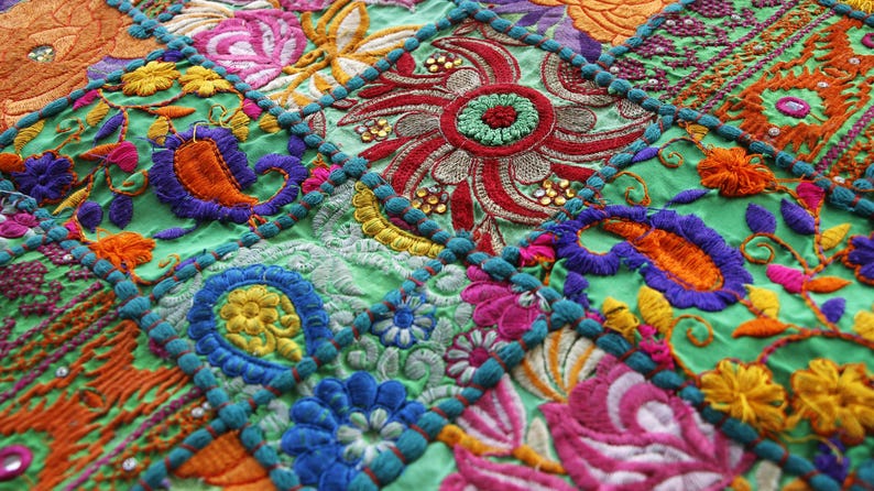 Pu&ograve; includere: Primo piano di un tessuto ricamato colorato con un design patchwork. Il tessuto presenta intricati motivi floreali e paisley nelle tonalit&agrave; di verde, arancione, viola, rosa e blu. Il design &egrave; incorniciato da un bordo turchese.