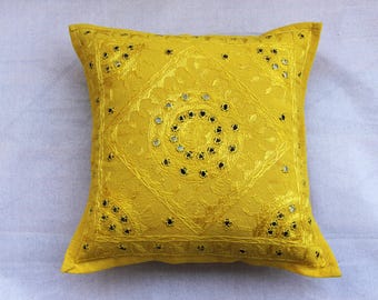 May include: Square yellow decorative pillow with intricate embroidered patterns and small mirrored accents. The pillow features a central diamond design and is likely used for home decor.