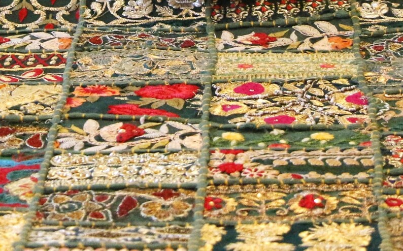 Puede incluir: Un tejido de color verde oscuro que presenta una cuadr&iacute;cula de parches rectangulares. Cada secci&oacute;n est&aacute; decorada con intrincados bordados en hilo dorado, rojo, blanco y naranja, con motivos florales, patrones geom&eacute;tricos y cuentas met&aacute;licas.