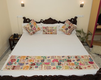 Puede incluir: Un juego de cama que incluye una colcha blanca, un camino de cama rectangular largo y tres cojines. Cada pieza está decorada con un diseño de patchwork colorido de patrones florales y geométricos bordados en varios colores vivos.