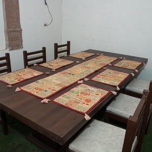 Puede incluir: Una mesa de comedor de madera marr&oacute;n oscuro con seis sillas que tienen cojines de color gris claro. La mesa est&aacute; decorada con un camino de mesa rectangular largo y seis manteles individuales a juego, todos con un patr&oacute;n de patchwork multicolor.