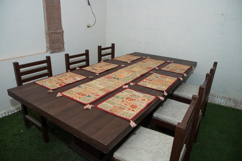 Puede incluir: Una mesa de comedor de madera marr&oacute;n oscuro con seis sillas que tienen cojines de color gris claro. La mesa est&aacute; decorada con un camino de mesa rectangular largo y seis manteles individuales a juego, todos con un patr&oacute;n de patchwork multicolor.