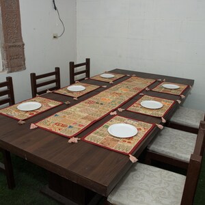 Puede incluir: Una mesa de comedor rectangular de madera marr&oacute;n oscuro con seis sillas a juego que tienen cojines de color claro. La mesa est&aacute; puesta con un camino de mesa rectangular de patchwork y seis manteles individuales a juego, cada uno con un plato blanco.