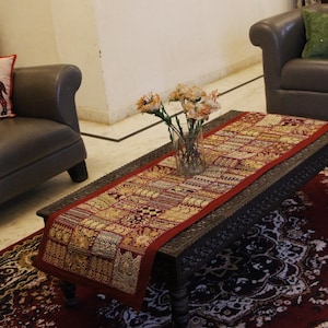 May include: A living room scene with a dark wood coffee table and a decorative runner. There's a grey leather armchair with a cushion, and a grey leather sofa. A patterned rug and a vase of flowers complete the decor.