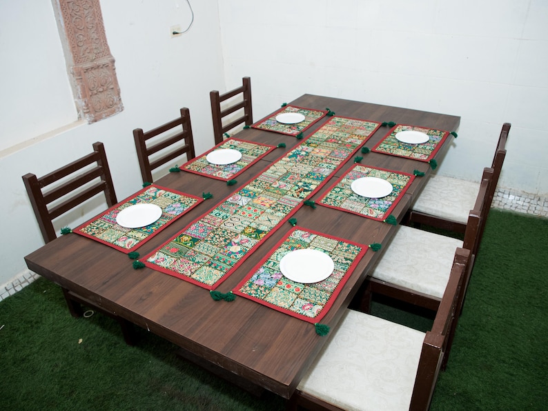 Puede incluir: Una mesa de comedor rectangular de madera marr&oacute;n oscuro con seis sillas de asientos tapizados en blanco. La mesa est&aacute; decorada con un camino de mesa de patchwork multicolor y seis manteles individuales rectangulares a juego con borlas verdes.