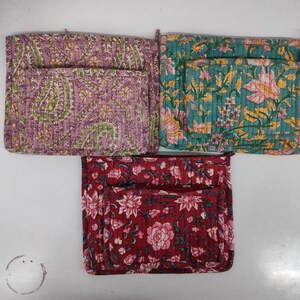 May include: Three quilted fabric pouches with floral and paisley patterns. The pouches are in shades of purple, teal, and red. Each pouch has a pocket on the front. The pouches are likely used for storage or organization.