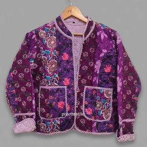 Puede incluir: Chaqueta acolchada morada con diseños florales y dos bolsillos delanteros. La chaqueta tiene cuello redondo y está forrada con una tela a rayas. Los puños y el ribete también son a rayas. La marca "preette textile" es visible.