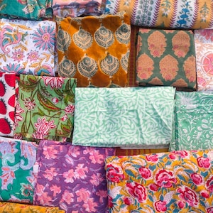 Può includere: Una collezione di quadrati di tessuto piegati con vari motivi floreali e geometrici. I colori includono turchese, rosa, giallo, verde e viola. I tessuti sembrano essere di cotone o un materiale simile, adatti per progetti di quilting o artigianato.